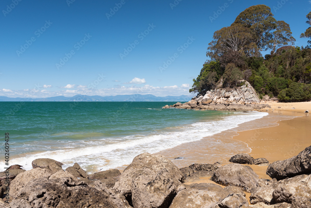 The sandy beach at Breaker Bay, with Kaka Point in the background and rocks in the foreground. Kaiteriteri, New Zealand.