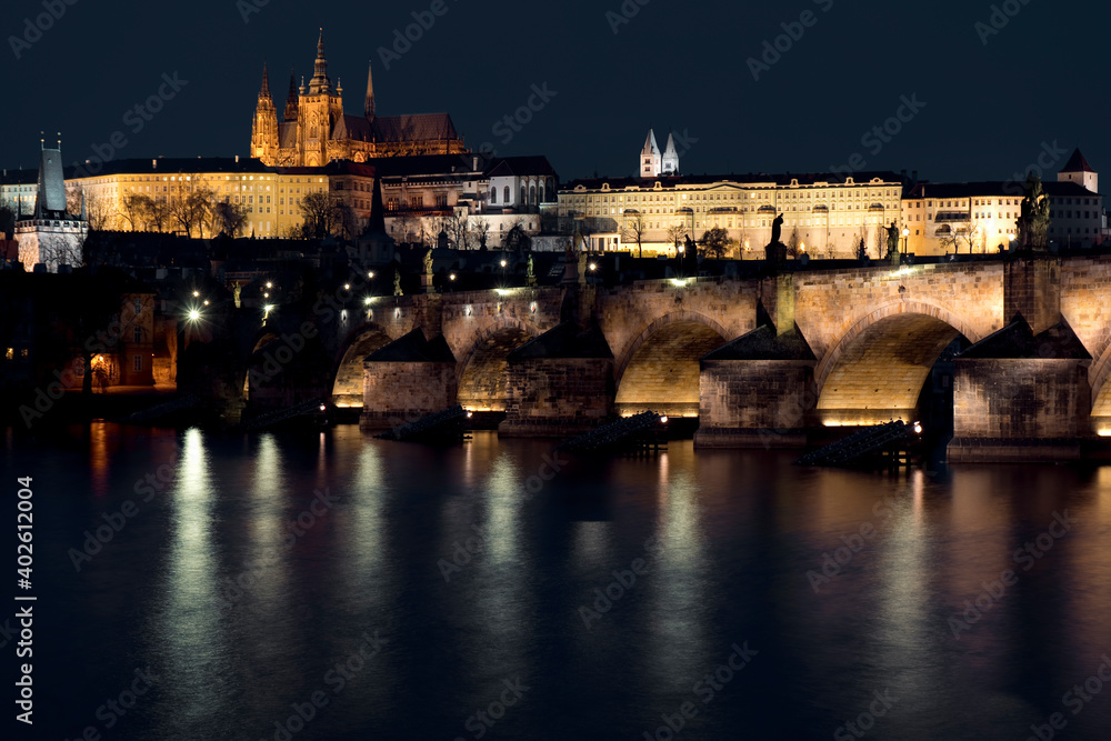 prague castle and charles bridge and st. vita church lights from street lights are reflected on the surface of the vltava river in the center of prague at night in the czech republic