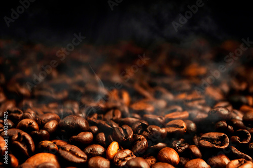 Coffee beans with roasting smoke. The concept of making aromatic strong coffee on a black background in a low key. Discreet photography.