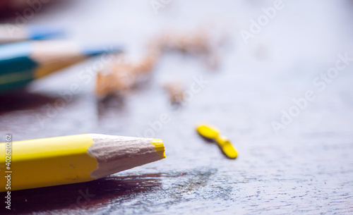 yellow broken color pencil on wooden table in blurry blue sharped pencil at background. artistic idea, develop art in aducation concept. colorful art wallpaper photo