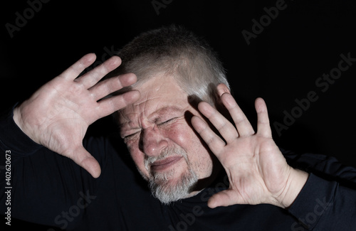 Ein älterer Mann wird von starkem Licht geblendet, er versucht sich mit den Händen zu schützen
