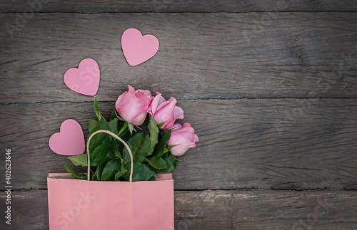 roses in a paper bag and heart on a wooden background.