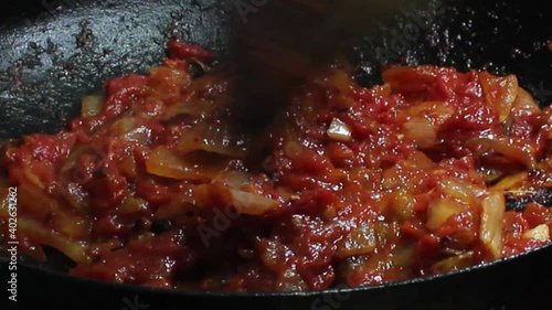 Frying tomato and onion in a fry pan with closeup view.