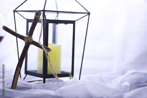 Religious concept. Handmade wooden cross on a white background. Wine glass lamp with candles. © alexkich