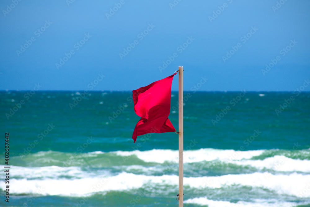 Red danger warning lifeguard safety flag waving in windy weather on the
