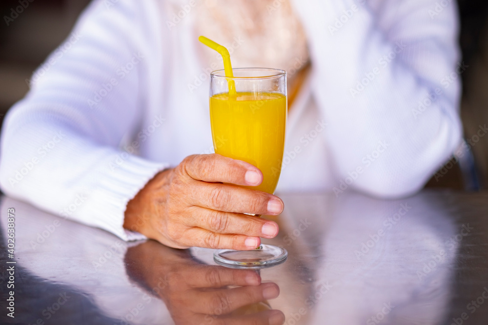 Natural orange juice in the hands of a senior woman sitting at the cafe table Natural orange juice in the hands of a senior woman sitting at the cafe table