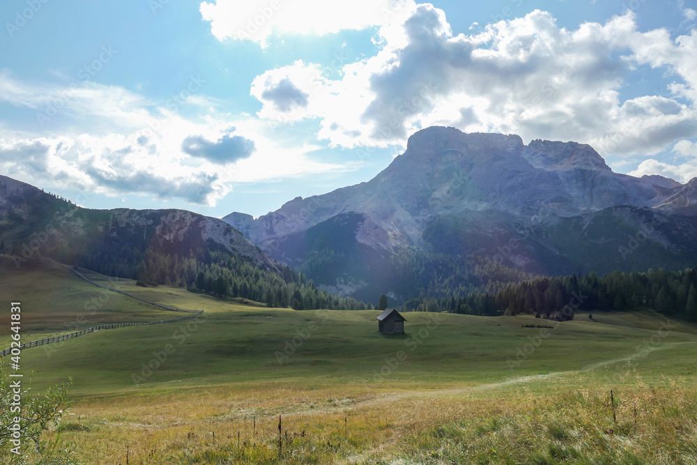 A panoramic view on the high Italian Dolomites from the top of Strudelkopf. There is a wide gravelled path leading to the top. Sunny day. A few clouds above the high peaks. Lush green plateau around A panoramic view on the high Italian Dolomites from the top of Strudelkopf. There is a wide gravelled path leading to the top. Sunny day. A few clouds above the high peaks. Lush green plateau around
