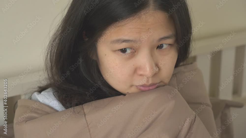 Sick infected Asian woman sitting in bed, at home, covered in blanket, having cold, shaking, looking outside lonely. Indoors, handheld, high angle view, pull out, close up shot, Covid-19 concept Sick infected Asian woman sitting in bed, at home, covered in blanket, having cold, shaking, looking outside lonely. Indoors, handheld, high angle view, pull out, close up shot, Covid-19 concept