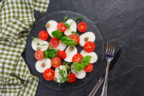 traditional caprese salad on a dark plate. Tomatoes with mozzarella cheese with basil on a dark background.