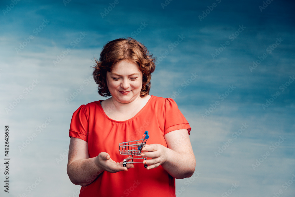 Young attractive plump woman with red hair looks at the little cart from the store in her hands. Young attractive plump woman with red hair looks at the little cart from the store in her hands.