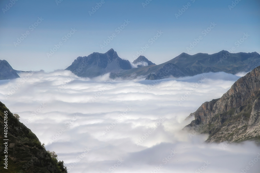 a sea of clouds runs through a glacial valley surrounded by high mountains
