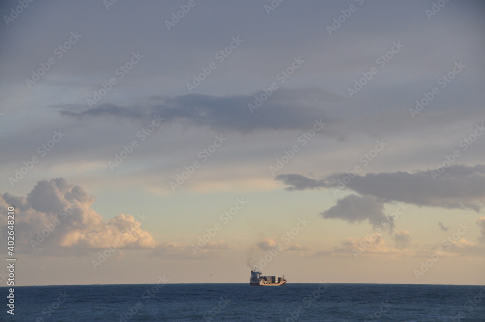 a lonely ship moored out of Genoa harbor at sunset with a cloudy sky seen from Nervi promenade, Liguria, Italy