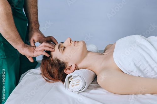 Face massage. Male hands make head massage to a beautiful young woman. Close-up of a woman getting spa treatment