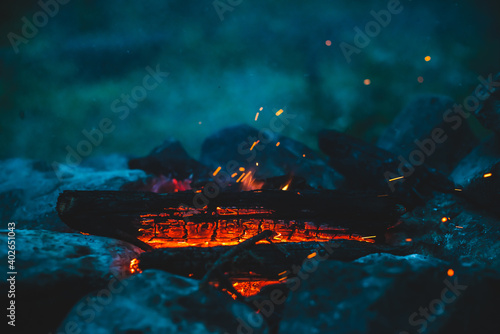 Vivid smoldered firewoods burned in fire close-up. Atmospheric warm background with orange flame of campfire and blue smoke. Unimaginable full frame image of bonfire. Burning logs in beautiful fire. photo