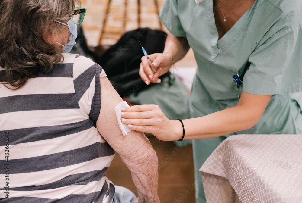 Nurse with medical protection white mask puts the coronavirus vaccine on elderly woman. All world make injections for people. Injection liquid for safe life