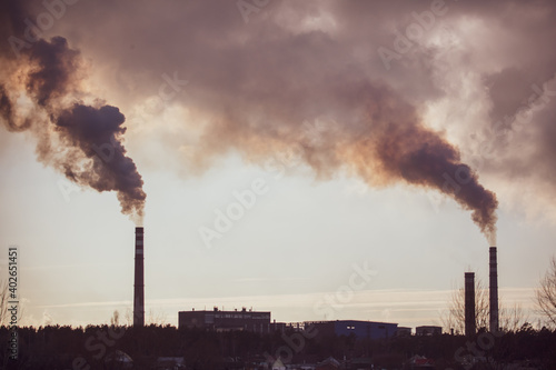 Smoke from chimneys at the plant in the rays of the sunset as a background.