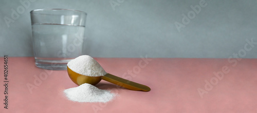 Gold measuring spoon with collagen and glass of water on pastel pink gray background. Horizontal banner for website or social networks with space for text. Powdered hydrolyzed fish collagen supplement