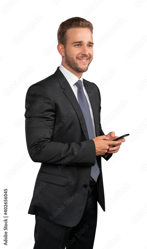 Businessman in black suit, white shirt and tie standing with phone in hands, isolated over white background. Caucasian manager smiling, looking away Businessman in black suit, white shirt and tie standing with phone in hands, isolated over white background. Caucasian manager smiling, looking away