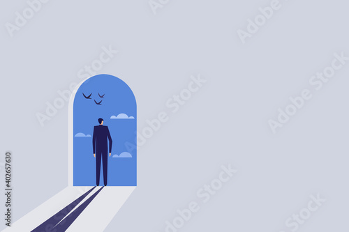 Businessman standing on a door opened to a blue sky filled with clouds and birds
