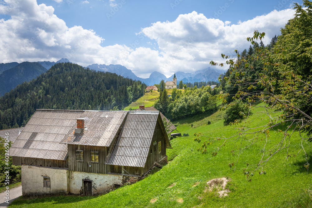 Obraz premium Church Cerkev Sveti Duh in Solčava with mountain range Kamnik Savinja Alps in Slovenia on a sunny summer day.