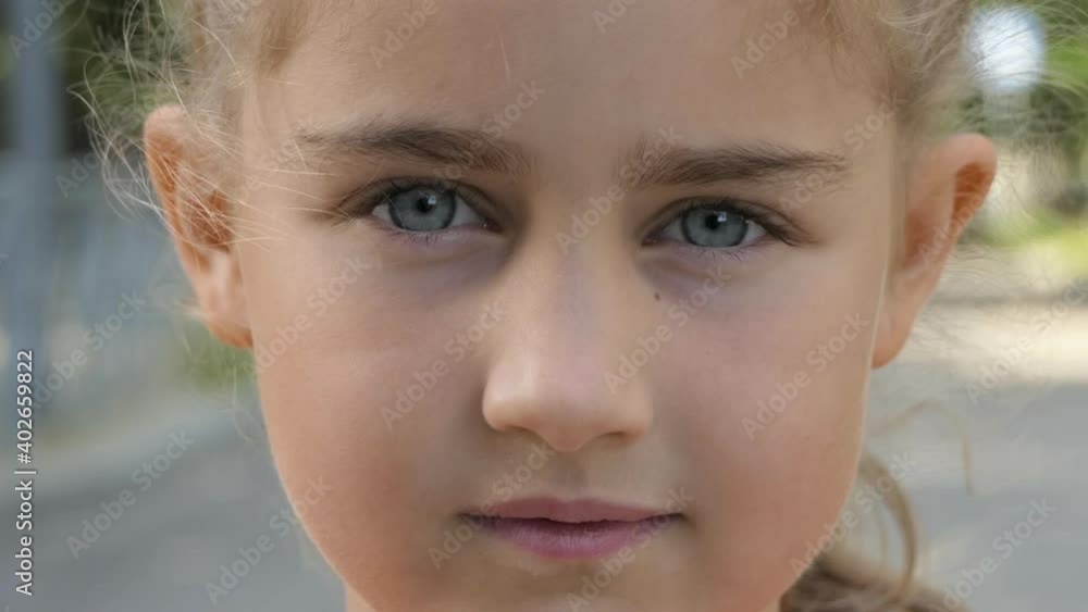 Portrait Little Child Girl Looking at Camera Standing on Street in City on Summer Day. Young Serious Thinking Curiosity Child Looking at Camera Closeup Outdoors. Face Eyes Serious Contemplative Child. Portrait Little Child Girl Looking at Camera Standing on Street in City on Summer Day. Young Serious Thinking Curiosity Child Looking at Camera Closeup Outdoors. Face Eyes Serious Contemplative Child.