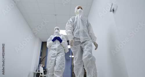 Dedicated medics in protective suits going along clinic corridor to fight with coronavirus infection