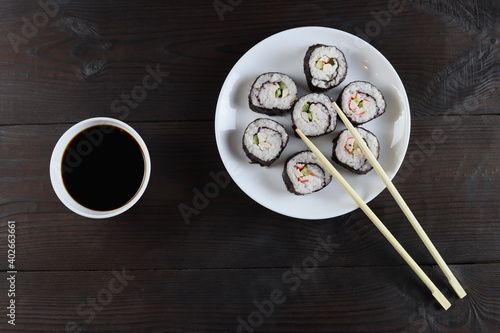 Set of fresh a sushi rolls in a white plate and soy sauce on a wooden table, top view