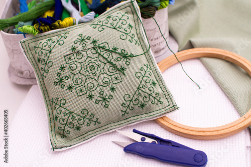 A pillow with embroidery lies next to a box of thread