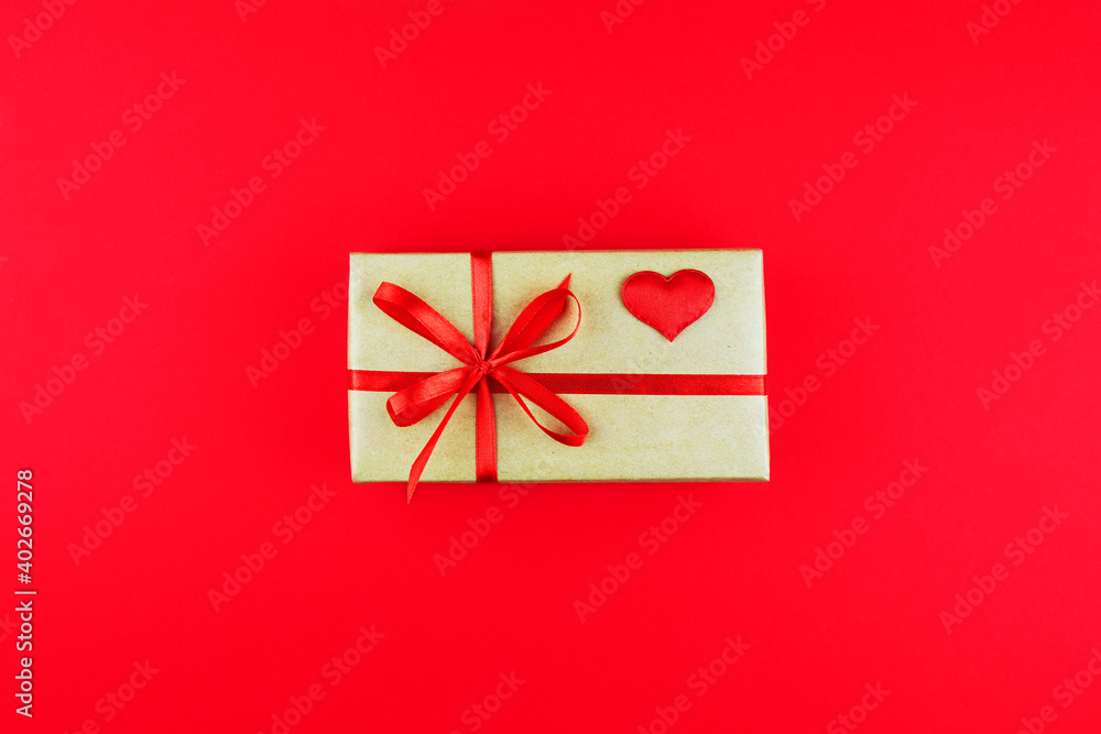 Gift box in a craft paper package with a red ribbon on a red background. Valentine's Day, Mother's Day, Birthday, Christmas. Gift box in a craft paper package with a red ribbon on a red background. Valentine's Day, Mother's Day, Birthday, Christmas.
