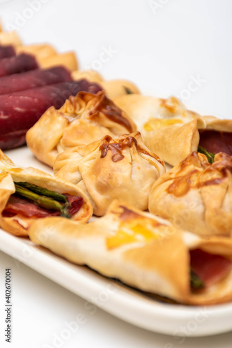 Vertical macro view of canapés and sachets with vegetables and ham and a pair of waiter's tongs. New concept of Mediterranean cuisine