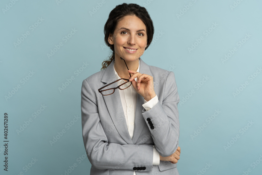Confident businesswoman holding glasses, smiling, looking at camera posing isolated on blue background Confident businesswoman holding glasses, smiling, looking at camera posing isolated on blue background