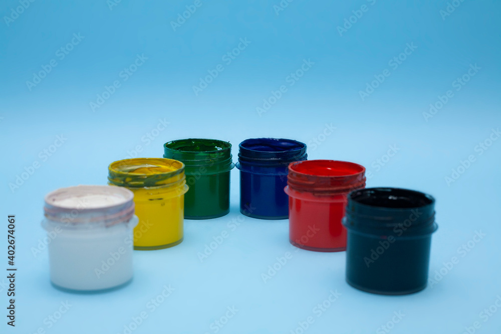 Plastic jars with multicolored paints on a blue background. Several colours of gouache, acrylic paint for drawing. For children’s creativity. Plastic jars with multicolored paints on a blue background. Several colours of gouache, acrylic paint for drawing. For children’s creativity.