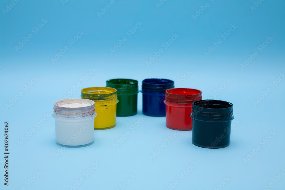 Plastic jars with multicolored paints on a blue background. Several colours of gouache, acrylic paint for drawing. For children’s creativity. Plastic jars with multicolored paints on a blue background. Several colours of gouache, acrylic paint for drawing. For children’s creativity.