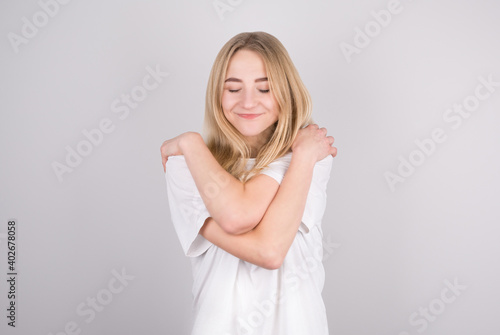 Portrait of lovely cheerful girl hugging herself enjoying life isolated on gray background