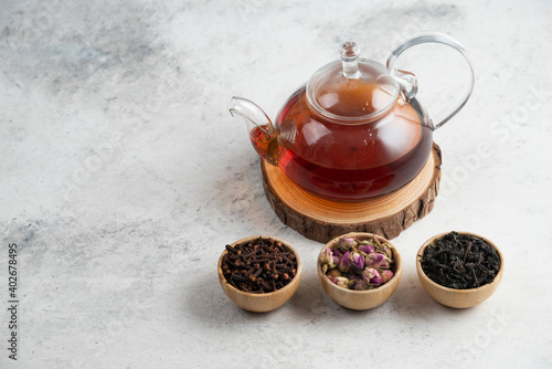 A glass teapot with wooden bowls of loose teas