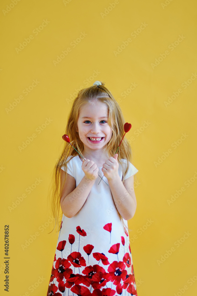 Little girl holding two little red hearts. The concept of Valentine's Day. Yellow background.