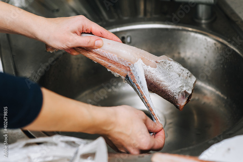 The girl cook cleans raw fish hake from the skins for cooking.