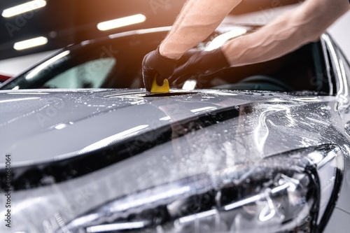 Obraz na płótnie Car detailing studio worker applying protective ppf foil film on car body and lamps w salonie