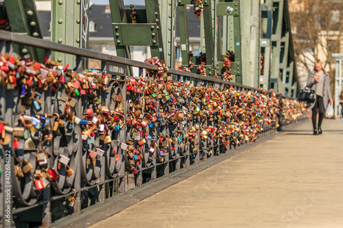 Many locks on the railing of the iron bridge in Frankfurt. Locks of love in different colors in the sunshine. Female person in the background
