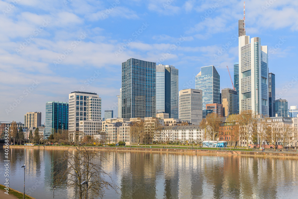 Frankfurt skyline on sunny day. River Main in the foreground. High-rise buildings from the financial district with reflections in the water. Blue sky with clouds