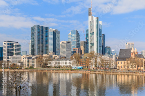 Frankfurt skyline on sunny day. River Main in the foreground. Commercial buildings from the financial district with reflections in the water. Blue sky with clouds