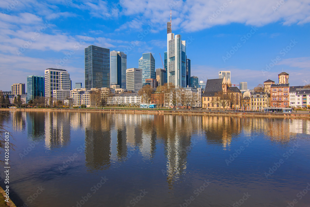 Financial district of Frankfurt am Main. River with reflections in the foreground on a sunny day. High-rise buildings for spring with blue sky and little clouds
