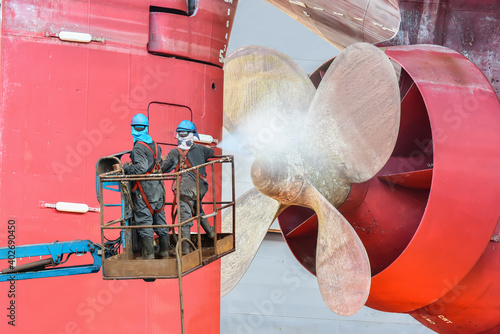 Washing and Cleaning propeller and rudder  Worker man on sherry picker car wear equipment protective PPE and safety harness in dry dock with water jet cleans the bottom of ship from sea vegetation