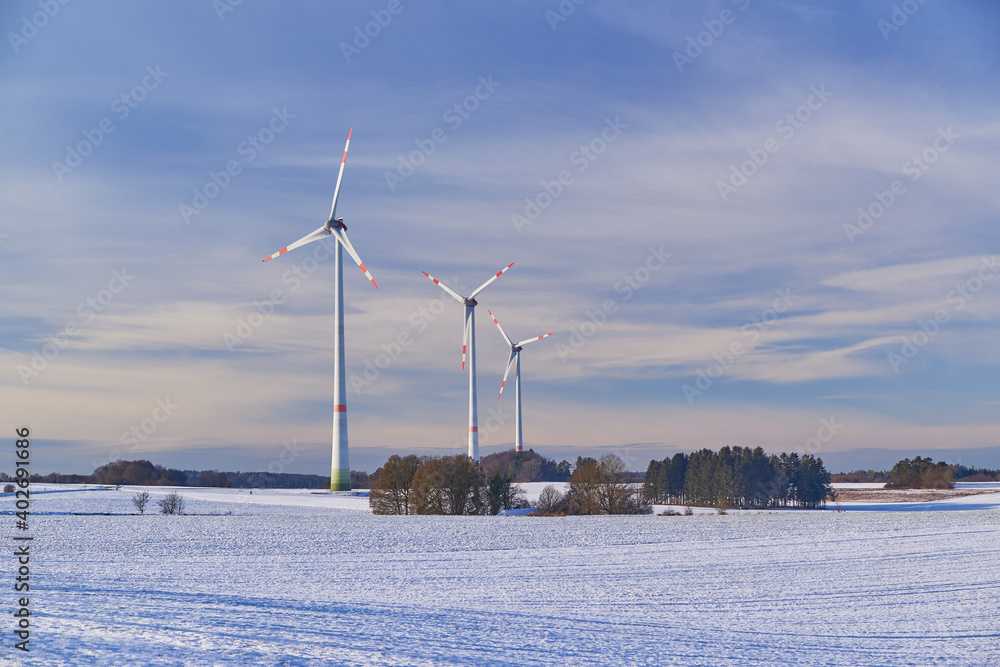 Fototapeta premium Windfarm on snowy farmland during sunset. Wind turbines on snowy farmland during sunset.