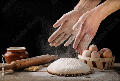 Man prepares bread dough on a wooden kitchen table.