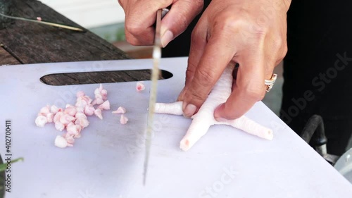 Female hand with knife cutting fingernails of chicken feet on kitchen white board photo