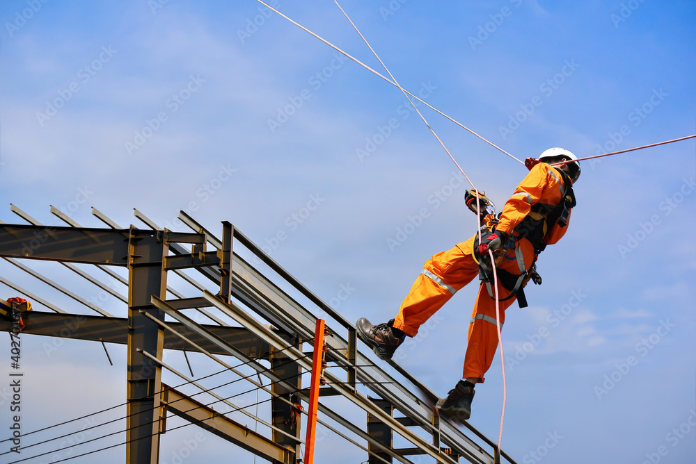 Safety sprinkling worker on high wear dresses and safety man with harness concept on steel structures success from work in site construction on blue sky background.