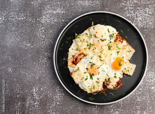 Fried eggs with bread, tomatoes and cheese on a round plate on a dark background. Top view, flat lay