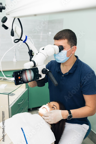 Dentist in latex gloves examining patient teeth in clinic. Patient lying with his open mouth in dentists office. Stomatologist performing examination using a microscope