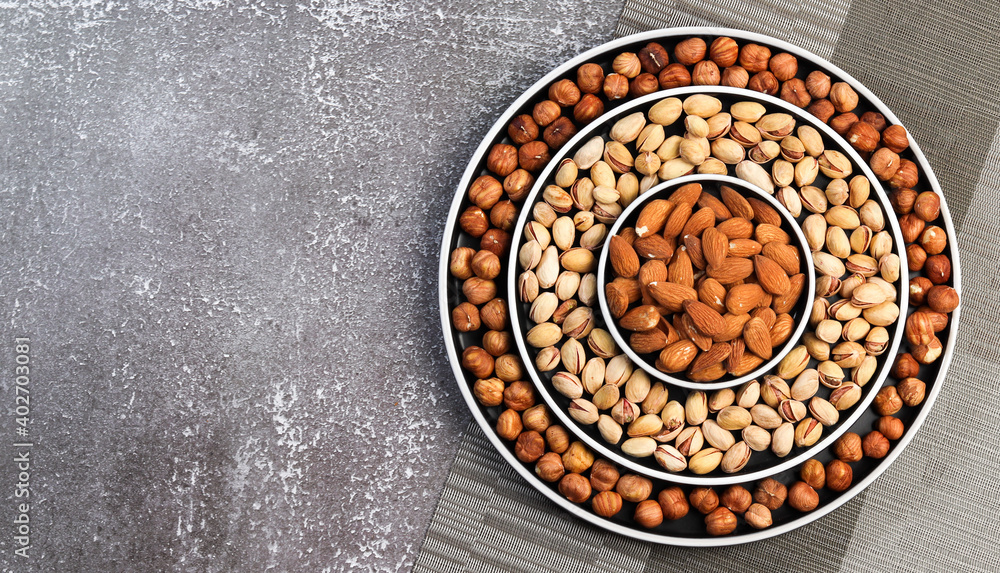 Assortment of various nuts in on a round plate on a dark background. Top view, flat lay